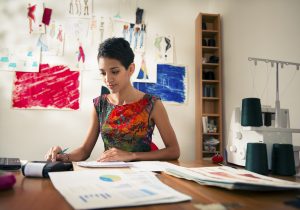 Money and financial planning, young hispanic self-employed woman checking bills and doing budget with calculator, computer and papers in fashion design studio