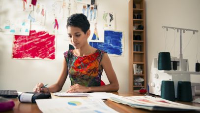 Money and financial planning, young hispanic self-employed woman checking bills and doing budget with calculator, computer and papers in fashion design studio