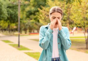 A young woman walking through a park in spring, rubbing her nose and looking uncomfortable because of allergies.
