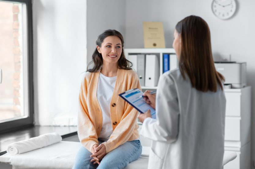 A dark haired woman in an orange cardigan having a consultation with a doctor during her hospital visit.