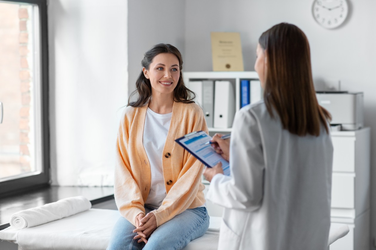 A dark haired woman in an orange cardigan having a consultation with a doctor during her hospital visit.