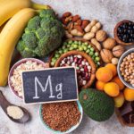 A small sign with the periodic symbol, Mg, written in chalk sits on top of a collection of magnesium-rich food.