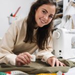 A young brunette woman smiling at the camera as she uses chalk to mark a piece of fabric for a sewing project.