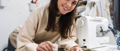 A young brunette woman smiling at the camera as she uses chalk to mark a piece of fabric for a sewing project.