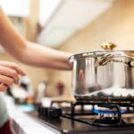 A young woman cooking dinner in a sauce pan on her gas stove. The stove's blue flame is visible.