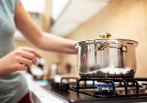 A young woman cooking dinner in a sauce pan on her gas stove. The stove's blue flame is visible.