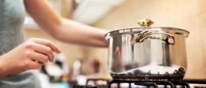A young woman cooking dinner in a sauce pan on her gas stove. The stove's blue flame is visible.