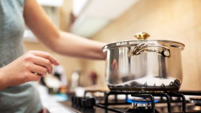 A young woman cooking dinner in a sauce pan on her gas stove. The stove's blue flame is visible.