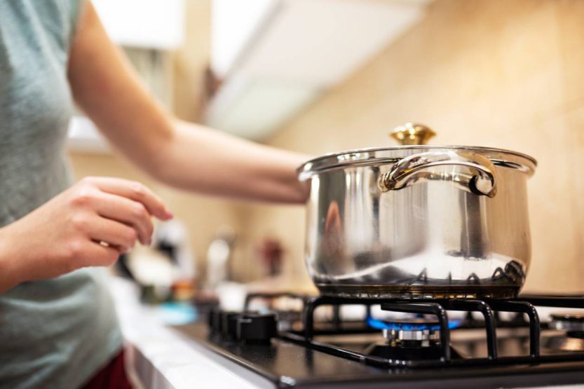 A young woman cooking dinner in a sauce pan on her gas stove. The stove's blue flame is visible.