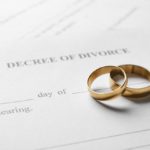 A paper that reads “decree of divorce” with two gold wedding bands stacked on each other resting on top of it.
