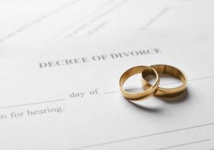 A paper that reads “decree of divorce” with two gold wedding bands stacked on each other resting on top of it.
