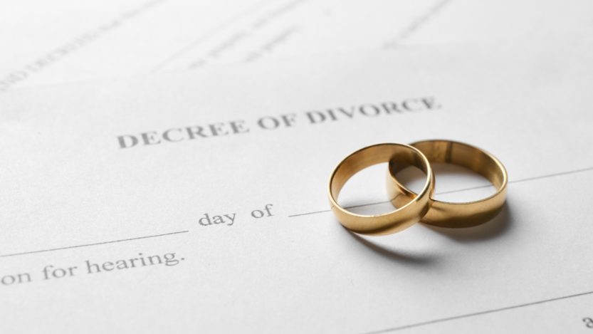 A paper that reads “decree of divorce” with two gold wedding bands stacked on each other resting on top of it.