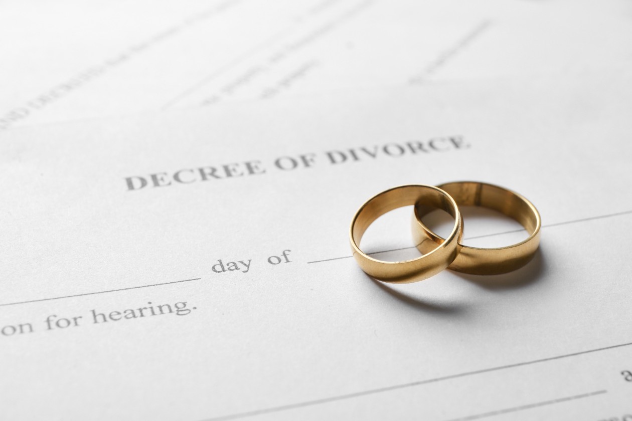 A paper that reads “decree of divorce” with two gold wedding bands stacked on each other resting on top of it.